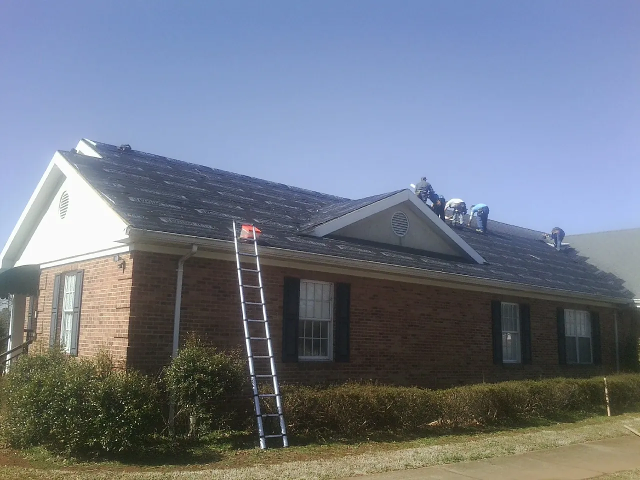 Crew tearing shingles off a brick ranch roof with a ladder set — Metal Roof Repair work by our crew in Mechanicsburg