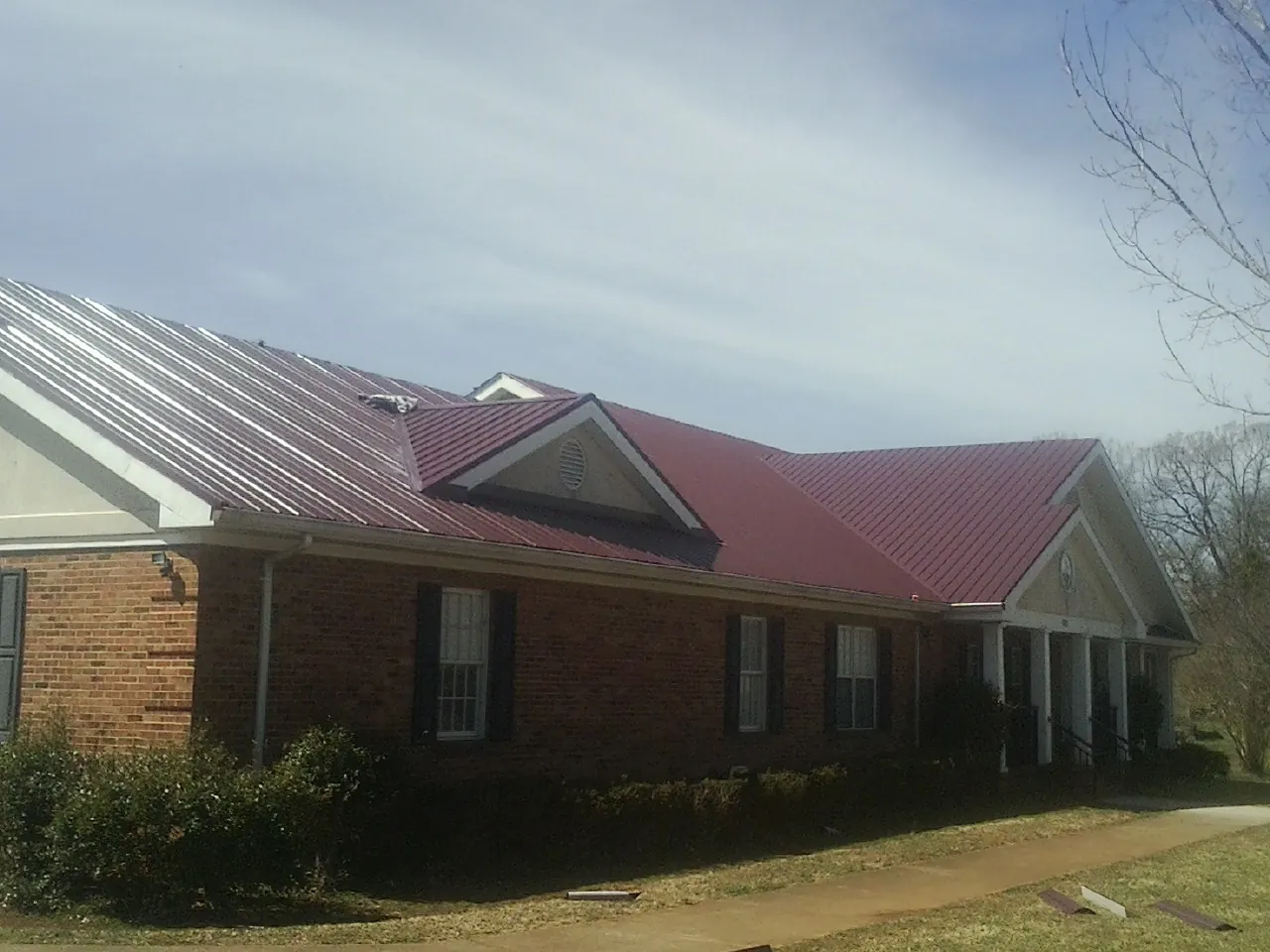 Red metal roof with gabled entries on a long brick building, from a Hail Damage Roof Repair job in Mechanicsburg