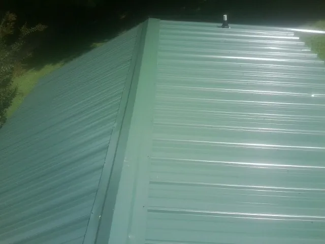 New green metal panels meeting at the ridge of a roof — Flat Roof Repair work by our crew in Mechanicsburg