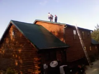 Crew on the ridge of a green metal roof on a two story log home in Mechanicsburg
